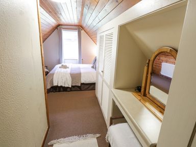 A narrow attic bedroom with a bed at the end and a small dressing table with mirror on the right at Bofin in Oughterard County Galway