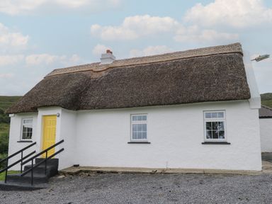 A white house with a thatched roof yellow door and stone steps in a rural area at Bofin in Oughterard County Galway