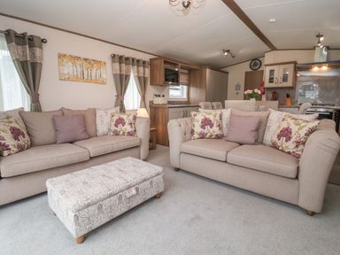 A living area with two beige sofas and floral cushions a patterned ottoman and a kitchen with dining chairs at Whispering Willows in Cayton Bay