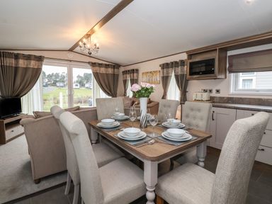 A dining area with a set table and chairs next to a living room with sofas and a television at Whispering Willows in Cayton Bay