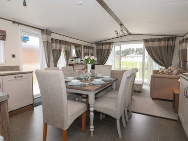 An open dining and living room with a dining table set for six and beige sofas at Whispering Willows in Cayton Bay