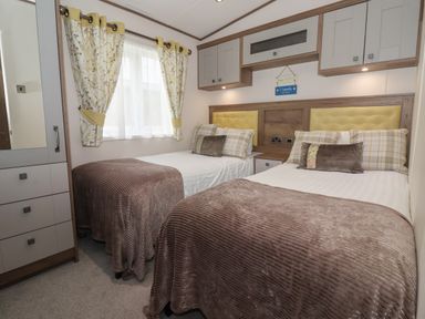 A bedroom with two single beds with brown blankets floral curtains and overhead cabinets at Whispering Willows in Cayton Bay