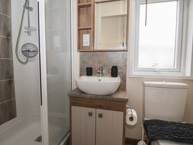 A bathroom with a shower, sink, mirror cabinet, toilet, and window at Whispering Willows in Cayton Bay