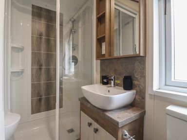 A bathroom with a shower, white basin, wooden cabinet, and a window at Whispering Willows in Cayton Bay
