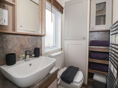 A bathroom with a sink a toilet and shelves with towels at Whispering Willows in Cayton Bay