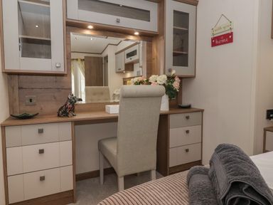 A bedroom dresser with a chair flowers a dog figurine and folded towels at Whispering Willows in Cayton Bay