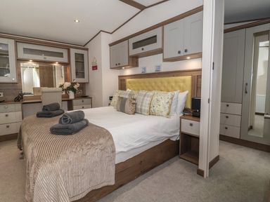 A bedroom with a double bed pillows and towels a dressing table with a mirror and chair at Whispering Willows in Cayton Bay