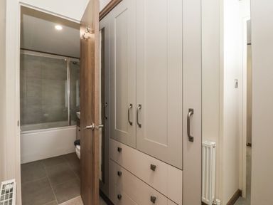 A hallway with a wardrobe and an open door showing a bathroom with a bathtub and sink at Whispering Willows in Cayton Bay