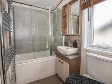 A bathroom with a bathtub shower combo sink with cabinet mirror window and toilet at Whispering Willows in Cayton Bay