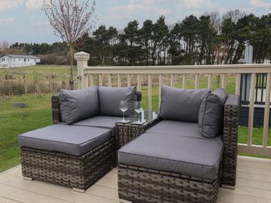 An outdoor seating area with two cushioned rattan chairs and a small glass-topped table on a wooden deck at Whispering Willows in Cayton Bay