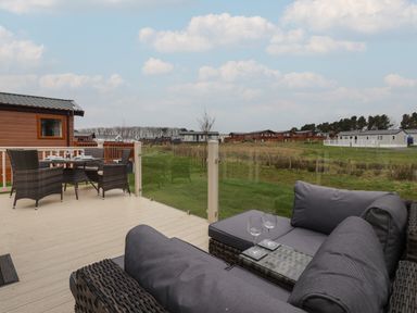 An outdoor deck with wicker seating and a table set with glassware overlooking a grassy area with multiple lodges at Whispering Willows in Cayton Bay