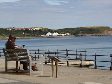 A statue sitting on a bench near the water at Whispering Willows in Cayton Bay