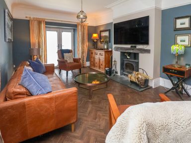 A living room with leather sofas a wood stove a television and a glass coffee table at The Manor House Skerry Vore Bryn Pydew near Llandudno Junction