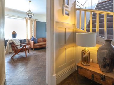 A hallway with a wooden bench lamp and vase next to carpeted stairs and a living room with armchair couch and window at The Manor House Skerry Vore Bryn Pydew near Llandudno Junction