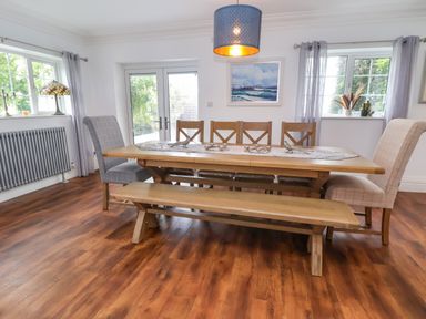 A dining room with a wooden table and bench with chairs by windows at The Manor House Skerry Vore Bryn Pydew near Llandudno Junction