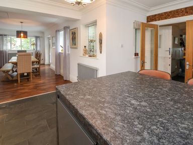 A dining area with a wooden table and chairs and a kitchen island with granite countertop at The Manor House Skerry Vore Bryn Pydew near Llandudno Junction