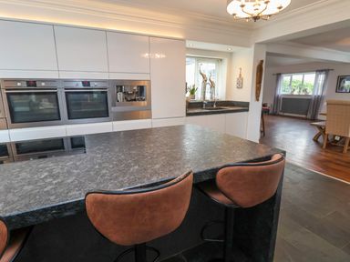A kitchen with built in ovens coffee machine stone countertop and brown bar stools at The Manor House Skerry Vore Bryn Pydew near Llandudno Junction