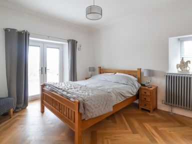 A bedroom with a wooden bed and bedside tables next to glass doors and a window at The Manor House Skerry Vore Bryn Pydew near Llandudno Junction