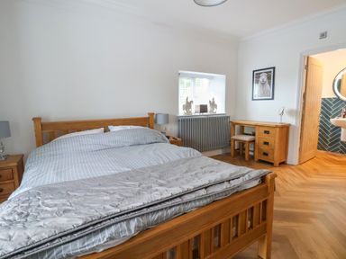 A bedroom with a wooden bed and side tables a desk with a stool a window with decorations and a door leading to a bathroom at The Manor House Skerry Vore Bryn Pydew near Llandudno Junction