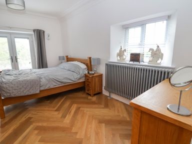 A bedroom with a wooden bed a bedside table lamps a window with blinds and a radiator at The Manor House Skerry Vore Bryn Pydew near Llandudno Junction