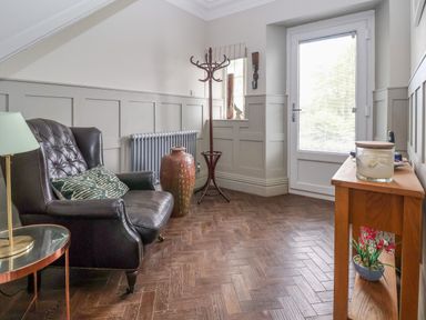 A room with a black leather armchair a wooden side table with a lamp and candle a coat rack and a large vase at The Manor House Skerry Vore Bryn Pydew near Llandudno Junction