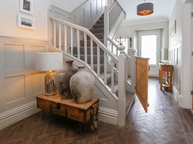 A hallway with a carpeted staircase a wooden table with large vases and a lamp and a wooden baby gate at The Manor House Skerry Vore Bryn Pydew near Llandudno Junction