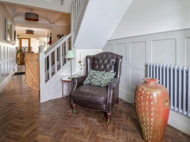 A hallway with a leather armchair and a patterned pillow next to a side table with a lamp and a large decorative vase at The Manor House Skerry Vore Bryn Pydew near Llandudno Junction