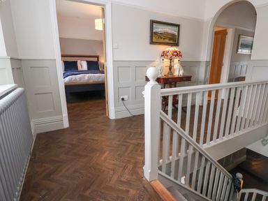 A hallway with wooden floor and white railing overlooking stairs with a bedroom and a small table with lamp and dog statues at The Manor House Skerry Vore Bryn Pydew near Llandudno Junction
