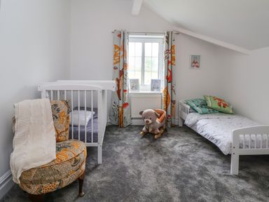 A children's bedroom with a crib, a toddler bed, a chair, a window with curtains, and a plush rocking dog at The Manor House Skerry Vore in Bryn Pydew near Llandudno Junction