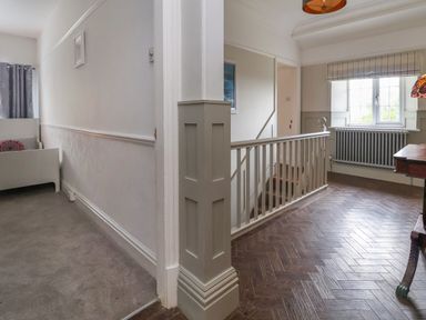 A hallway with carpeted floor and a small bed on the left and a staircase with a wooden railing and a window on the right at The Manor House Skerry Vore Bryn Pydew near Llandudno Junction