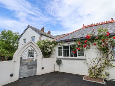 A white house with a slate roof and red flowers climbing on the wall next to a gated archway at The Manor House Skerry Vore in Bryn Pydew near Llandudno Junction