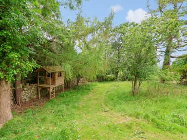 A grassy garden area with trees and a wooden playhouse on stilts at The Manor House Skerry Vore in Bryn Pydew near Llandudno Junction