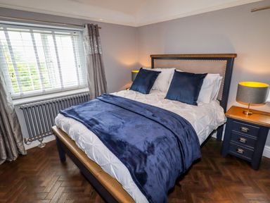 A bedroom with a bed with blue pillows and blanket beside a window and nightstand at The Manor House Skerry Vore in Bryn Pydew near Llandudno Junction