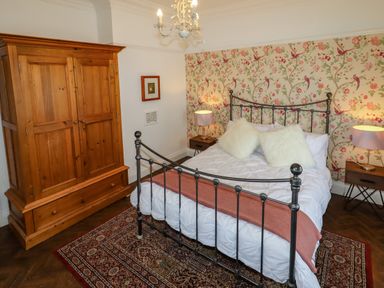 A bedroom with a metal framed bed two fluffy pillows a wooden wardrobe two bedside tables with lamps and floral wallpaper at The Manor House Skerry Vore Bryn Pydew near Llandudno Junction