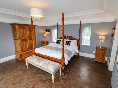 A bedroom with a wooden four poster bed two bedside tables with lamps a wooden wardrobe and a bench at The Manor House Skerry Vore Bryn Pydew near Llandudno Junction