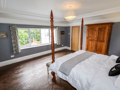 A bedroom with a four-poster bed and wooden wardrobe near a window at The Manor House Skerry Vore in Bryn Pydew near Llandudno Junction