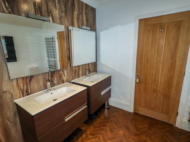 A bathroom with two sinks and mirrors next to a wooden door at The Manor House Skerry Vore Bryn Pydew near Llandudno Junction