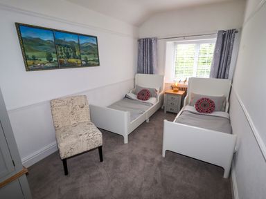 A bedroom with two single beds a chair and a nightstand with a lamp at The Manor House Skerry Vore in Bryn Pydew near Llandudno Junction