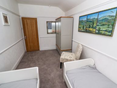 A bedroom with two single beds a wardrobe a patterned chair a mirror and landscape artwork on the wall at The Manor House Skerry Vore Bryn Pydew near Llandudno Junction
