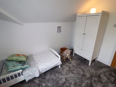 A child's bedroom with a small white bed with star-patterned bedding a white wardrobe a teddy bear rocker and a framed picture on the wall at The Manor House Skerry Vore in Bryn Pydew near Llandudno Junction