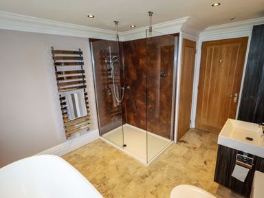 A bathroom with a glass shower enclosure a towel rack a wooden door and a sink at The Manor House Skerry Vore Bryn Pydew near Llandudno Junction