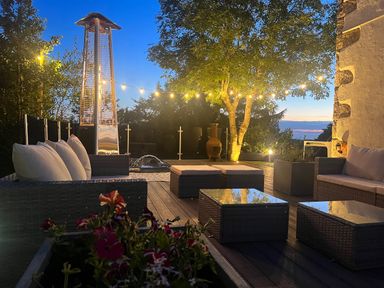 An outdoor seating area with wicker furniture a patio heater string lights and trees at The Manor House Skerry Vore Bryn Pydew near Llandudno Junction