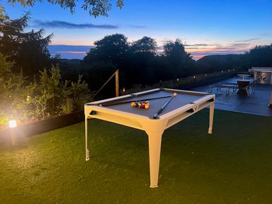 A pool table on grass with pool cues and balls at sunset with trees and outdoor furniture at The Manor House Skerry Vore in Bryn Pydew near Llandudno Junction