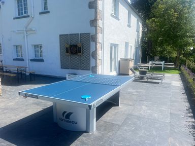 An outdoor patio area with a table tennis table bench seating dartboard sun loungers and trees at The Manor House Skerry Vore Bryn Pydew near Llandudno Junction