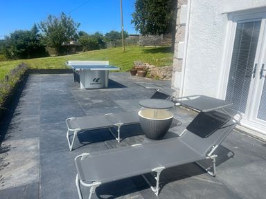 An outdoor patio with two gray lounge chairs a small round table and a ping pong table on dark tiled flooring at The Manor House Skerry Vore Bryn Pydew near Llandudno Junction