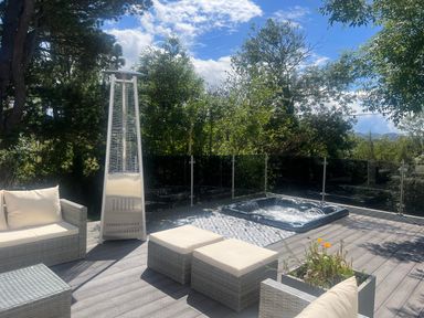 An outdoor patio with cushioned wicker furniture a tall heater a hot tub and trees in the background at The Manor House Skerry Vore Bryn Pydew near Llandudno Junction