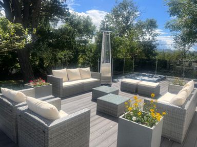 An outdoor patio with wicker sofas, two glass tables, a patio heater, planters with flowers, and a hot tub at The Manor House Skerry Vore in Bryn Pydew near Llandudno Junction