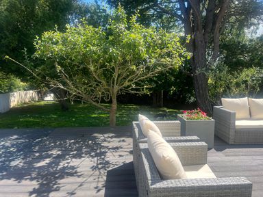 An outdoor patio with wicker chairs and a planter next to a grassy garden with trees at The Manor House Skerry Vore Bryn Pydew near Llandudno Junction