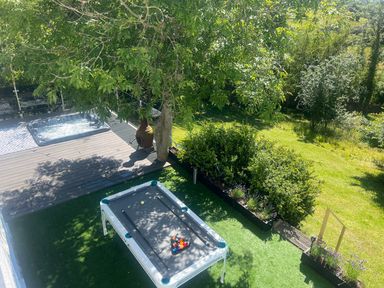 An outdoor area with a pool table on artificial grass a hot tub on a wooden deck green bushes and trees at The Manor House Skerry Vore in Bryn Pydew near Llandudno Junction