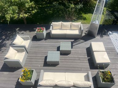 An outdoor patio with sofas, armchairs, ottomans, square planters with flowers, and a tall patio heater at The Manor House Skerry Vore in Bryn Pydew near Llandudno Junction